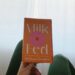 Milk Fed by Melissa Broder Book Review, holding up book, orange cover and window in background